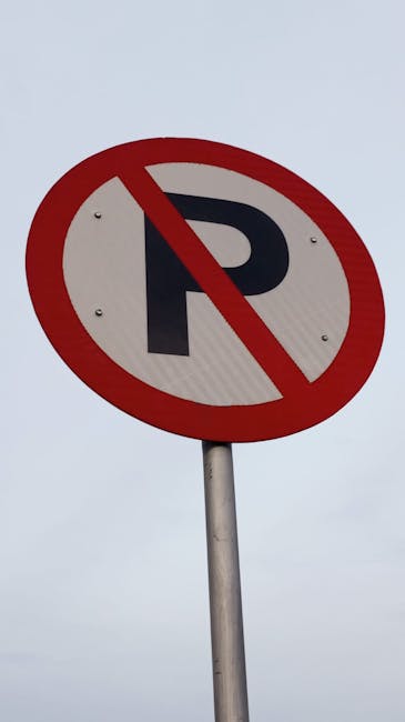 A circular no parking sign with a red border and a black letter 'P' crossed out by a red diagonal line, mounted on a silver metal pole against an overcast sky. The sign is situated outdoors, likely near a residential property or roadway, and is part of local regulations related to parking permits for house removals or moving services in Aldersbrook. This sign may be relevant for parking restrictions during a home relocation, where careful planning for furniture transport and loading logistics is necessary. The surroundings are not visible, but the sign’s placement suggests it is intended to inform drivers about parking limitations in the area to facilitate efficient removal or moving operations provided by companies like Man and Van Aldersbrook, which specialise in removals and relocation services.